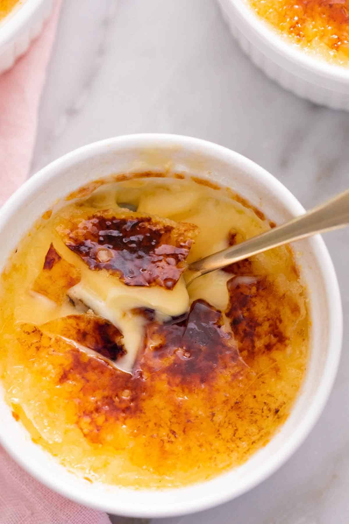 Overhead view of a crème brûlée, top is cracked, with a spoon inside.