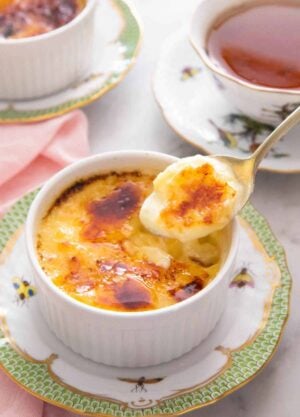 A spoonful of crème brûlée lifted from the ramekin with a cup of tea in the background.
