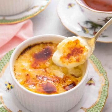 A spoonful of crème brûlée lifted from the ramekin with a cup of tea in the background.