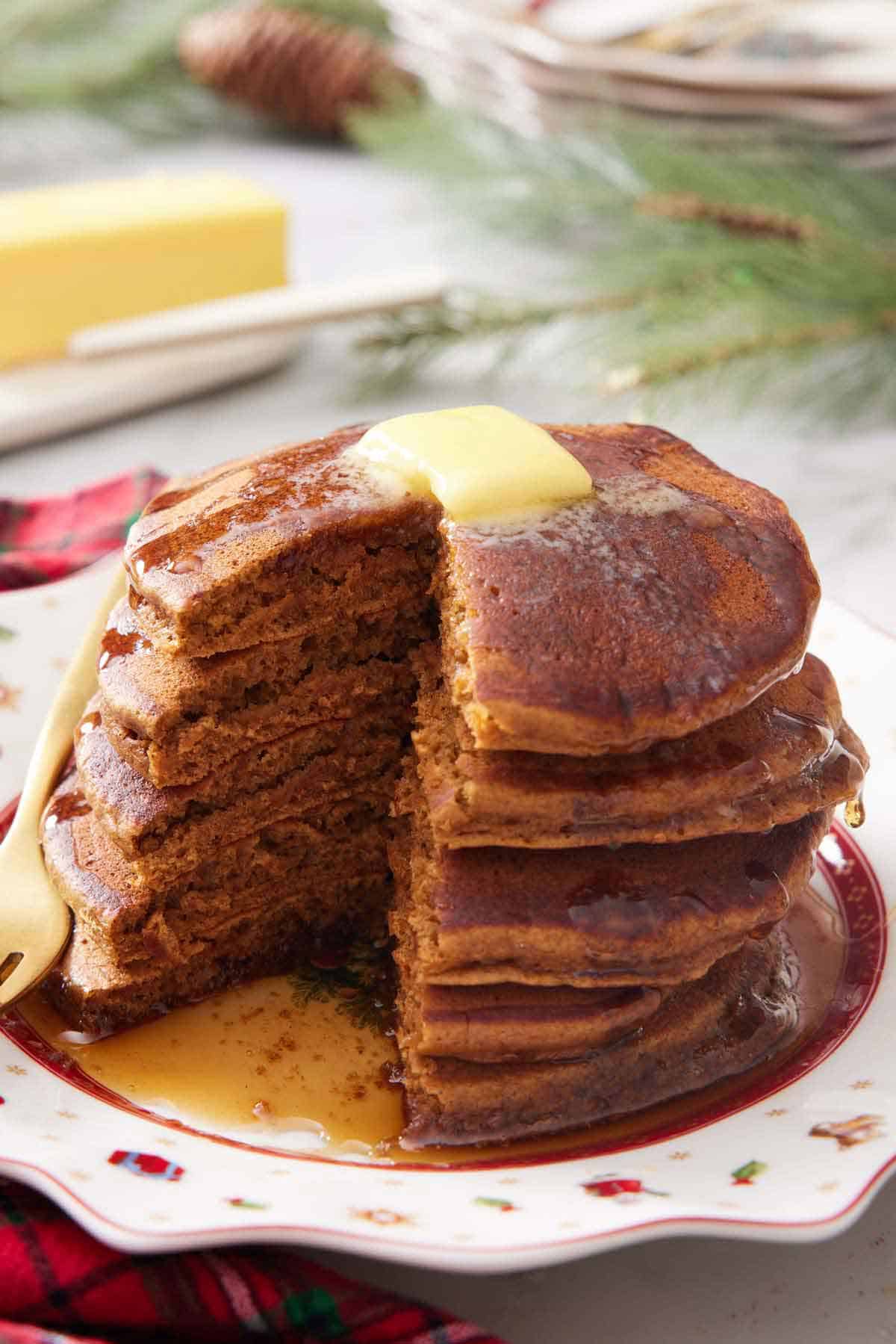 A stack of gingerbread pancakes with a portion cut out. Butter and syrup on top.