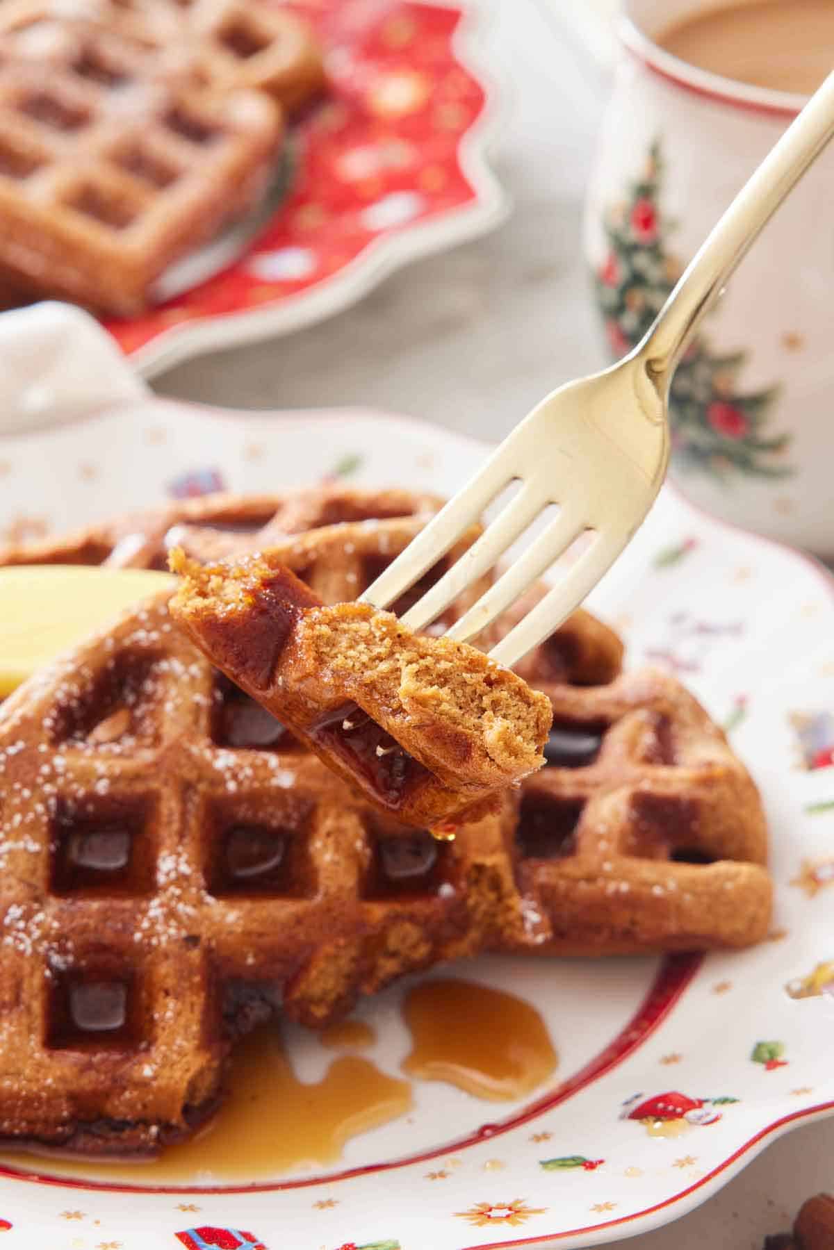 A fork lifting up a bite of gingerbread waffle from a plate.