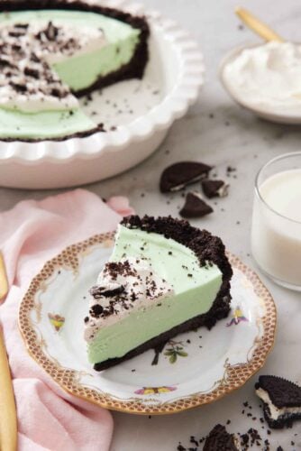 A slice of grasshopper pie on a plate with the rest in a baking dish in the background.
