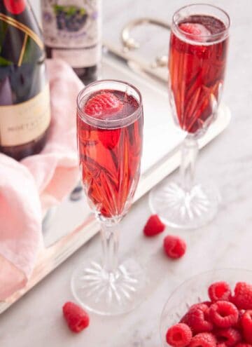 Two glasses of Kir Royale with a bowl of raspberries and the bottles of alcohol in the back.