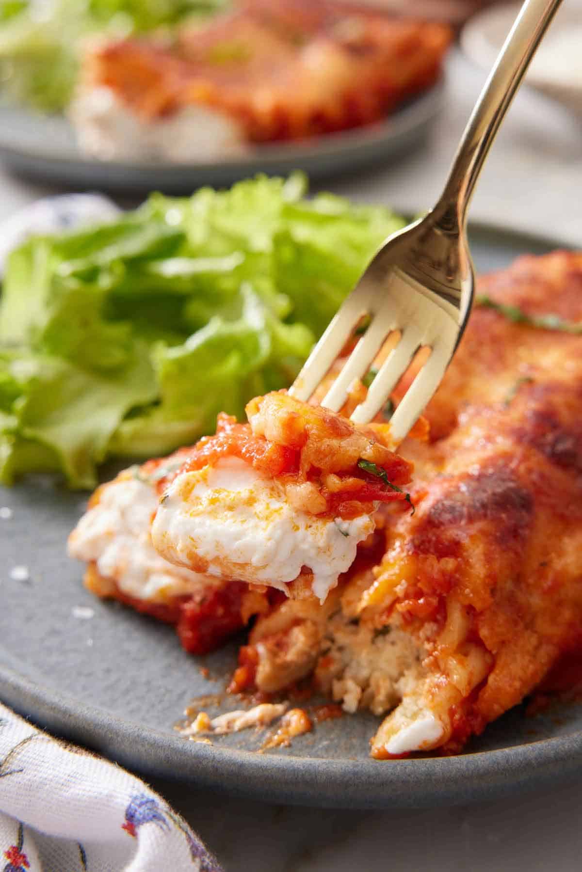 A fork lifting a bite of manicotti from a plate.