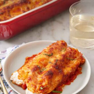 Pinterest graphic of a plate with manicotti with a baking dish and glass of wine in the background.