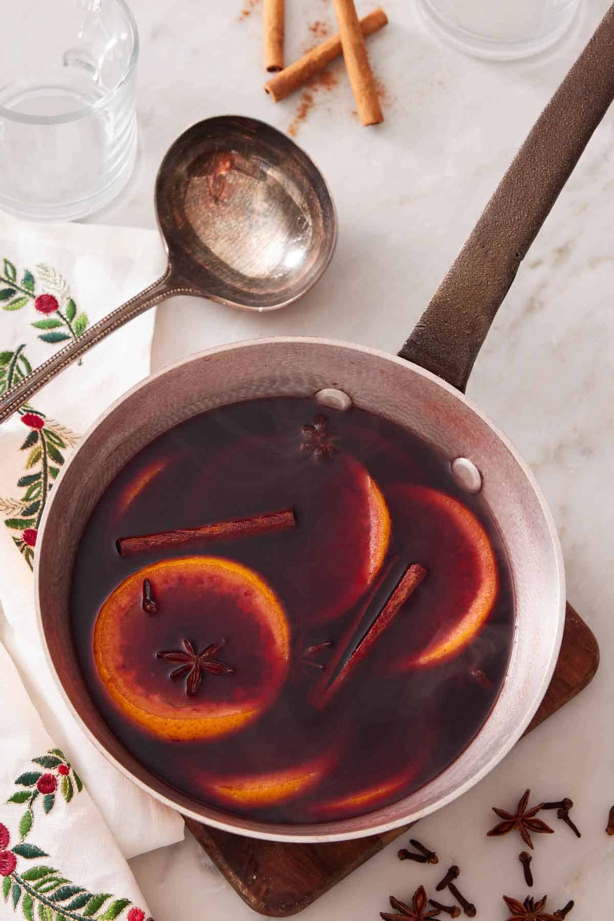 Overhead view of a skillet of mulled wine with a ladle off to the side. Scattered star anise around with cinnamon sticks.