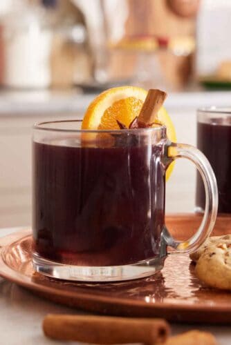 A glass of mulled wine with a cinnamon stick and orange slice garnish.