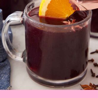Pinterest graphic of an orange slice placed into a glass of mulled wine.