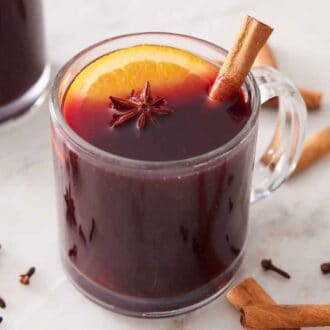 A glass of mulled wine with a cinnamon stick, star anise, and orange slice. More garnishes on the side.