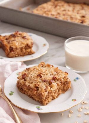 Two plated slices of oatmeal cake with a glass of milk and rest of the baking pan in the background.