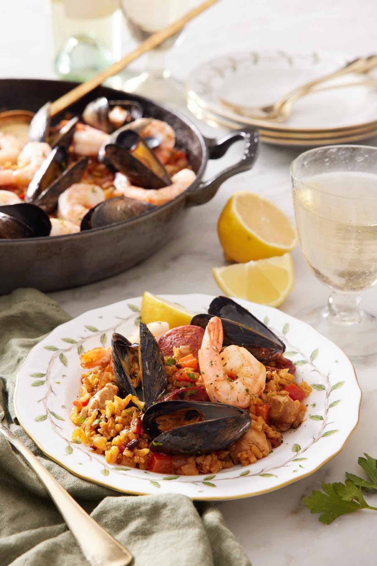 A plate of paella with a glass of wine and skillet of more paella in the background.