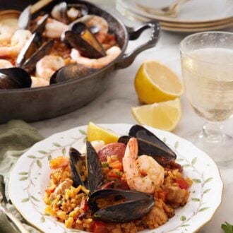 Pinterest graphic of a plate of paella with a glass of wine and skillet of more paella in the background.