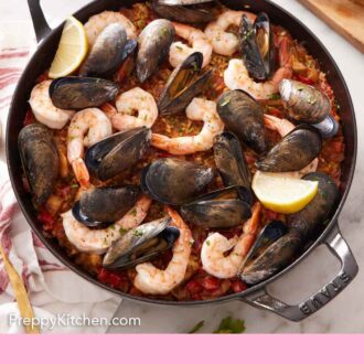 Pinterest graphic of an overhead view of a skillet of paella with cut lemons beside it.