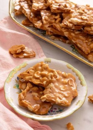 A plate of peanut brittle with a platter with more in the background.
