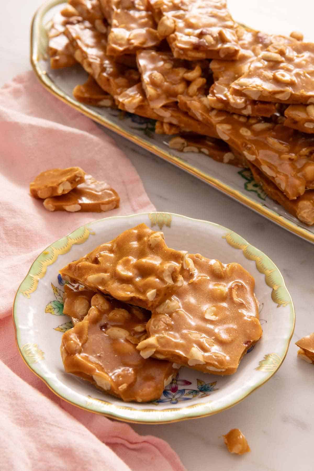 A plate of peanut brittle with a platter with more in the background.