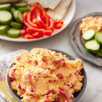 Pinterest graphic of a bowl of pimento cheese with some crackers, peppers, and cucumbers in the background.