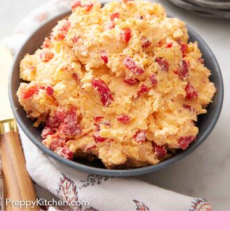 Pinterest graphic of a bowl of pimento cheese along with some crackers, peppers, and cucumbers.