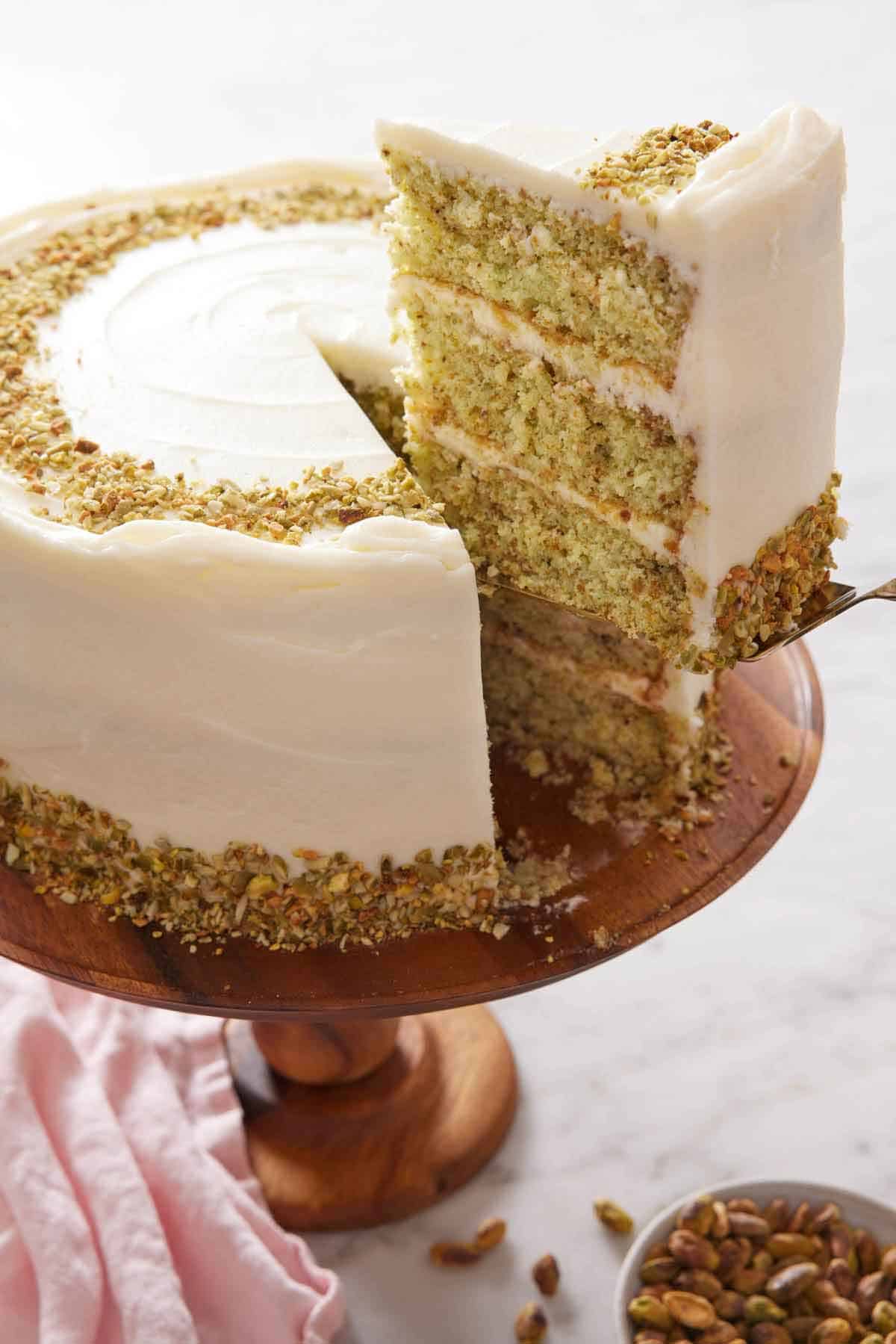 A slice of pistachio cake cut and lifted from the cake on the cake stand.