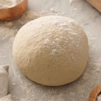 A ball of pizza dough on a marble surface with a dusting of flour on top.