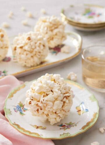 A popcorn ball on a plate with more balls in the background on a platter.