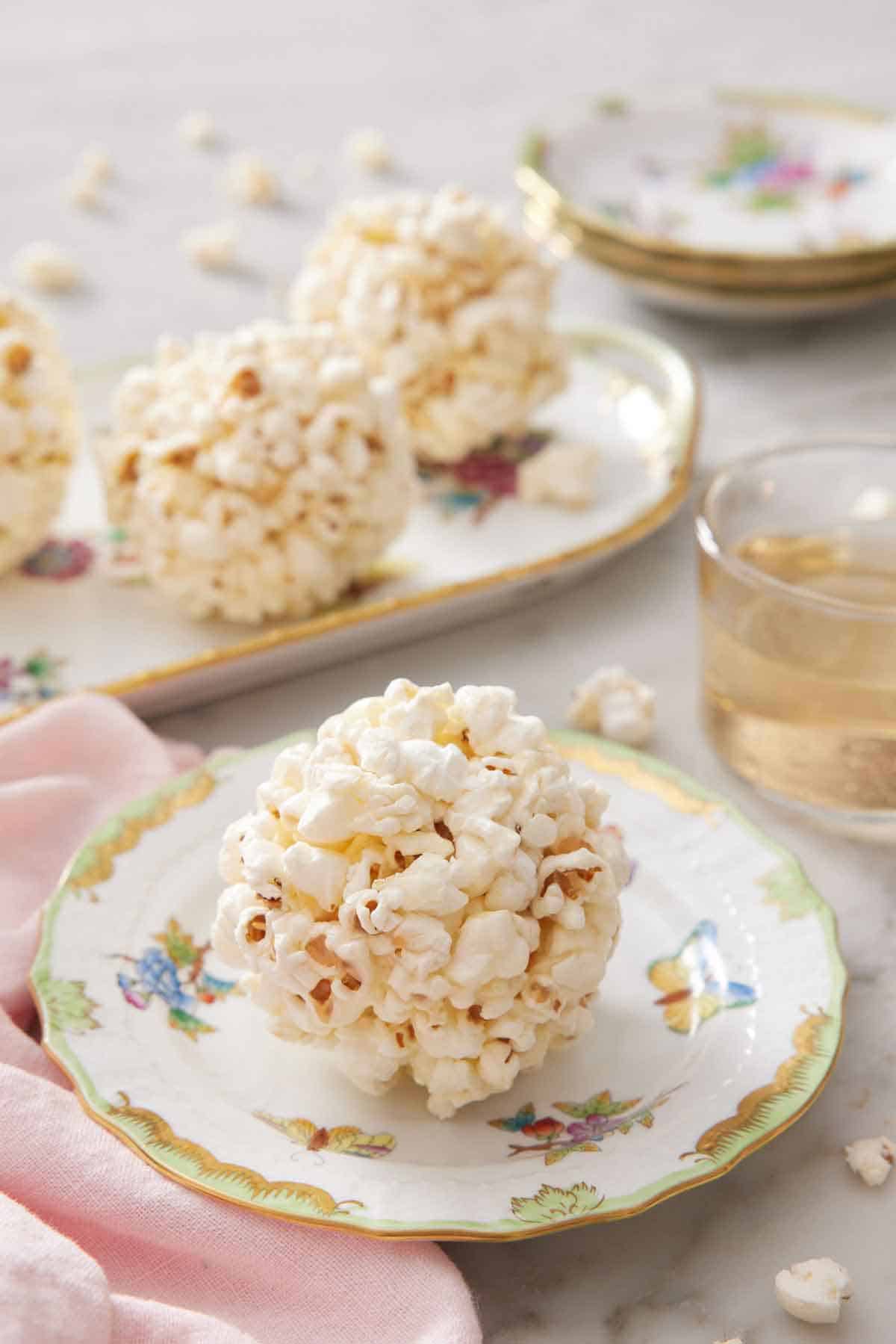 A popcorn ball on a plate with more balls in the background on a platter.