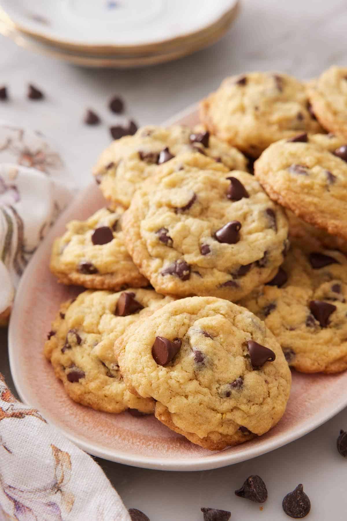 A platter of pudding cookies with some chocolate chips scattered around and a stack of plates in the background.