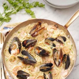 Pinterest graphic of a skillet of seafood pasta with a stack of plates and forks behind it along with parsley.