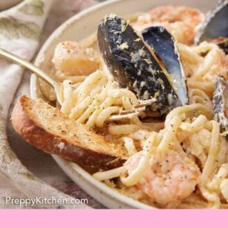 Pinterest graphic of a plate with seafood plate and toasted bread with a fork in the noodles.