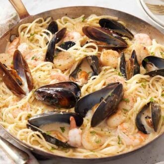 A skillet of seafood pasta topped with chopped parsley.