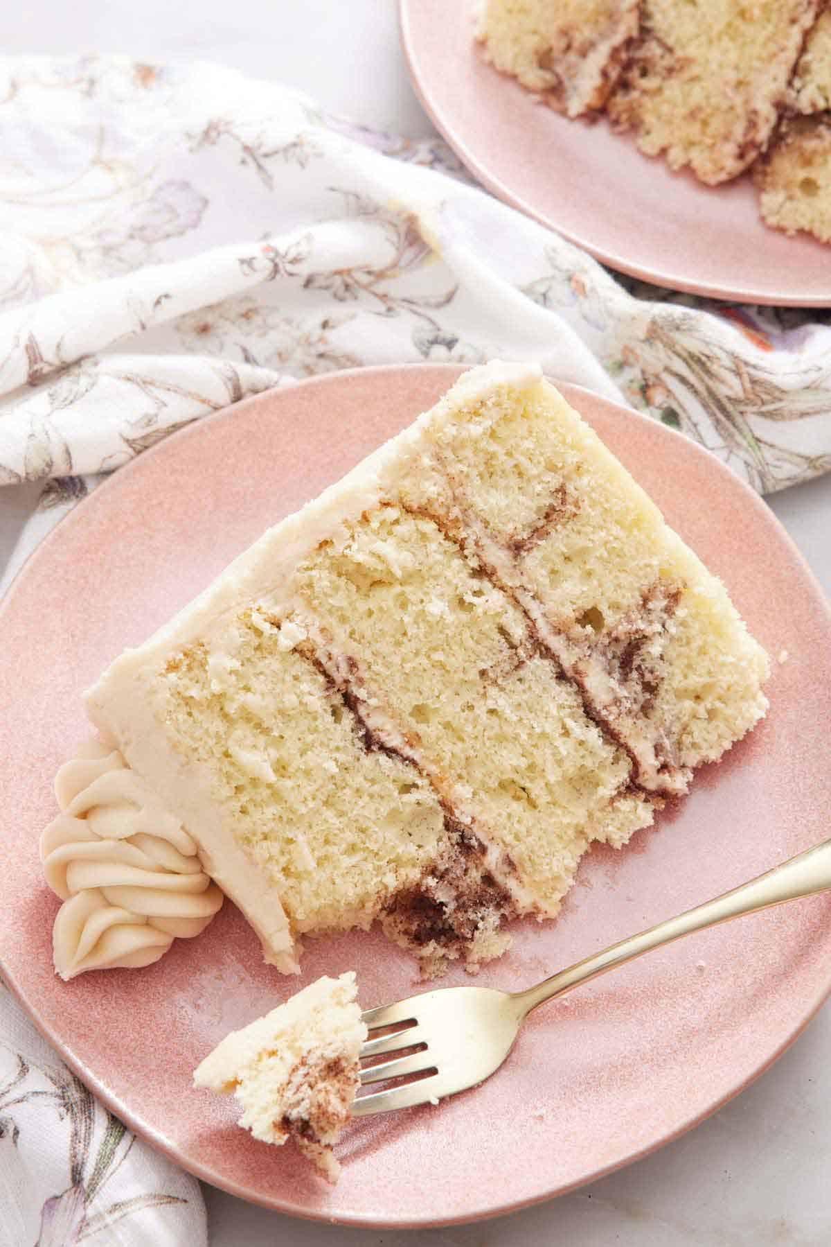 A slice of snickerdoodle cake on a pink plate, showing the three layers. A fork with a bite on it by the cake.