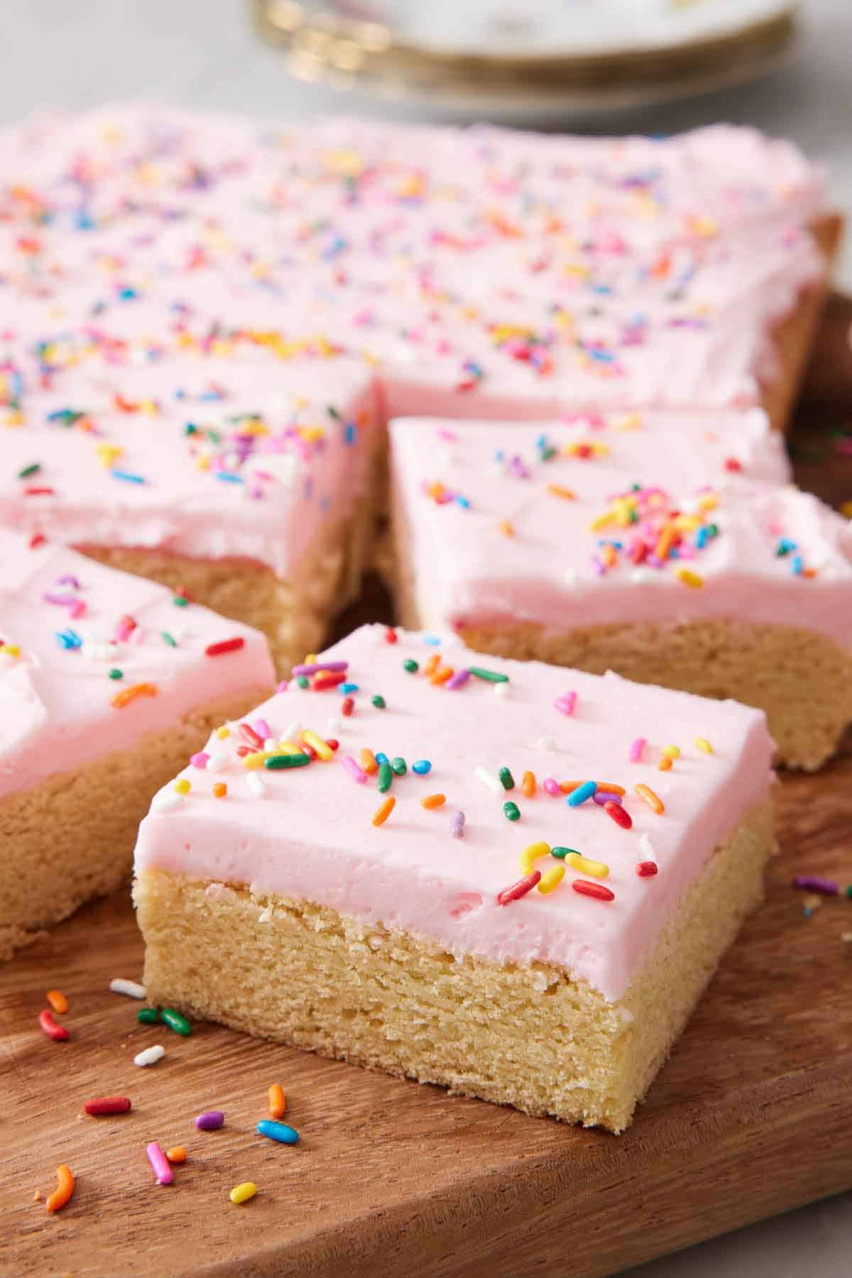 Sugar cookie bars on a wooden serving board, topped with rainbow sprinkles.