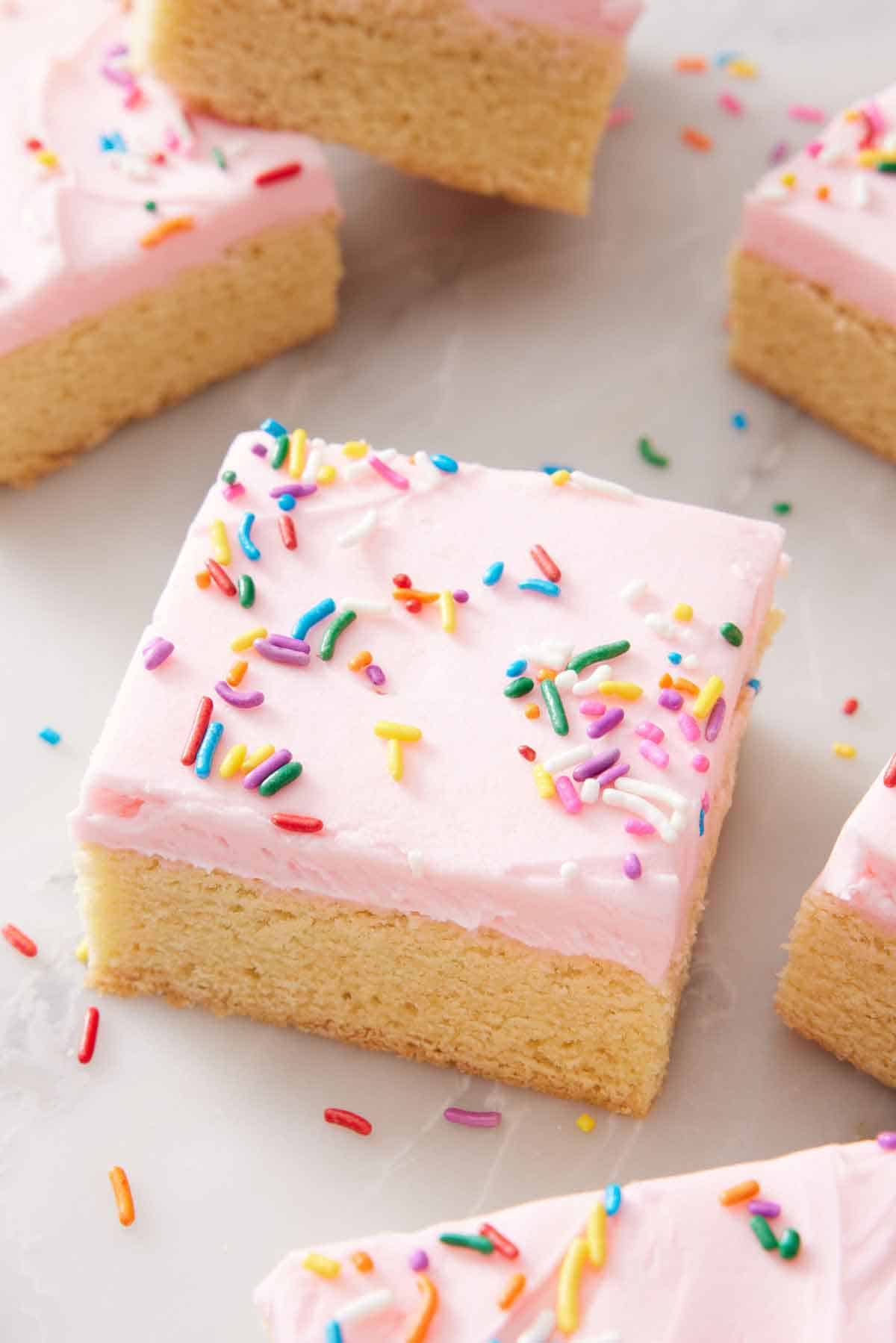 A slightly angled view of a cut sugar cookie bar with some off to the side, sprinkles scattered around.