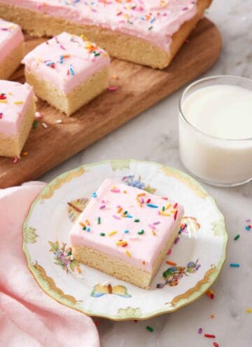 A plate with a sugar cookie bar with a glass of milk and additional sugar cookie bars in the background.