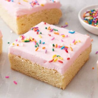 Four sugar cookie bars with one in the middle with a small bowl of sprinkles in the background.