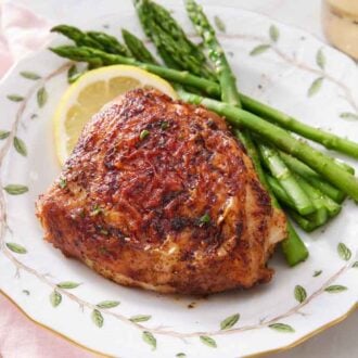 A plate with an air fryer chicken thigh with asparagus and lemon slice.