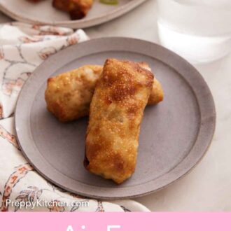 Pinterest graphic of a plate with two air fryer egg rolls with a glass of ice water and platter with more rolls in the background.