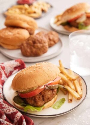 A plate of air fryer turkey burger with fries on the side with a glass of water in the background along with more burger ingredients.