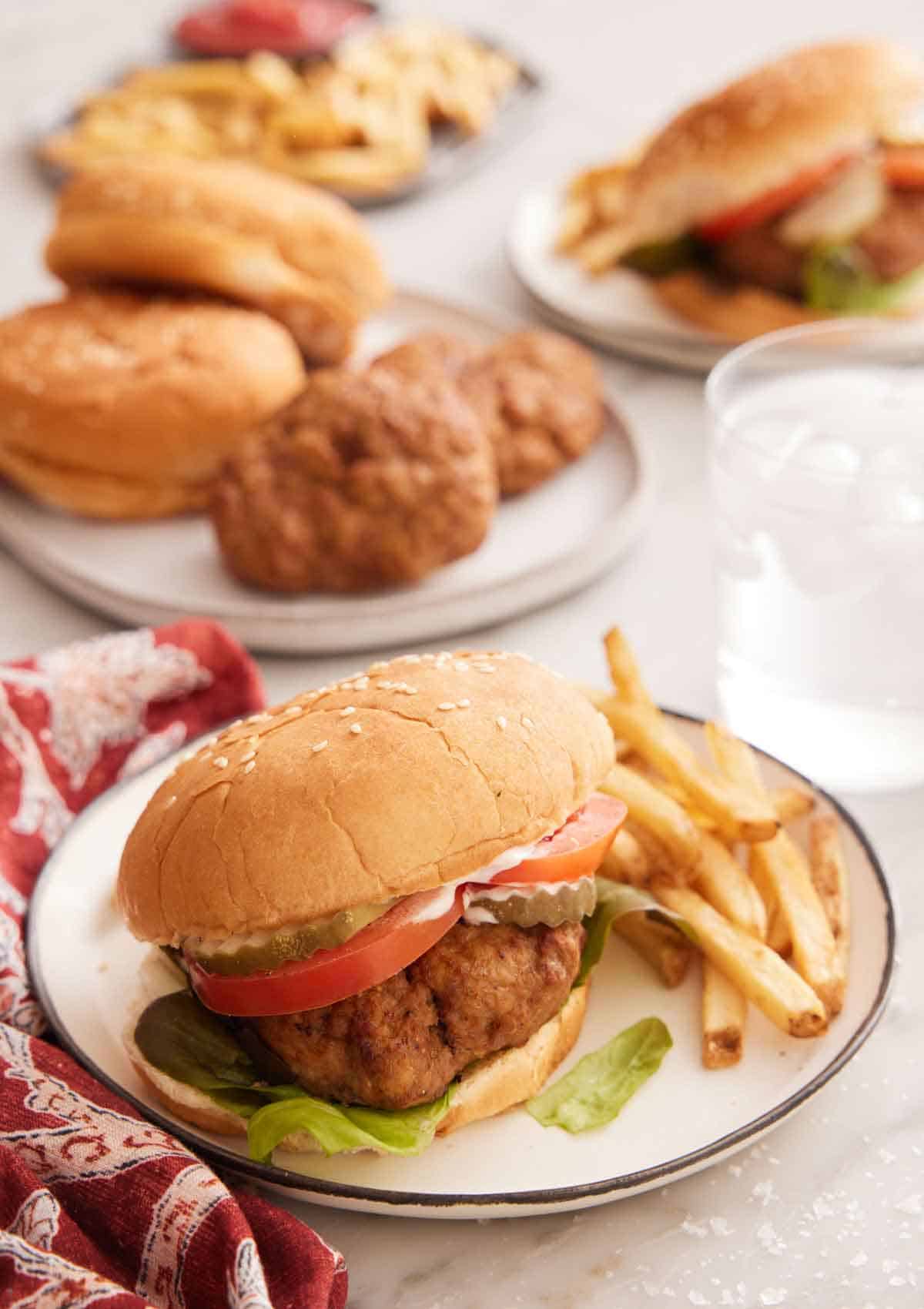 A plate of air fryer turkey burger with fries on the side with a glass of water in the background along with more burger ingredients.