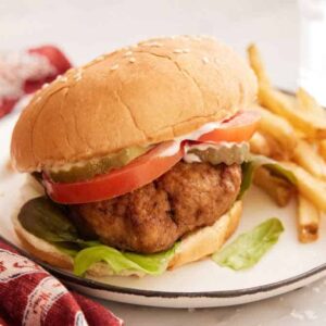 A plate with a air fryer turkey burger with a side of fries and a linen napkin beside it.
