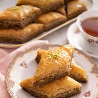 Pinterest graphic of a plate with three pieces of baklava with a cup of tea and tray of more baklava in the background.
