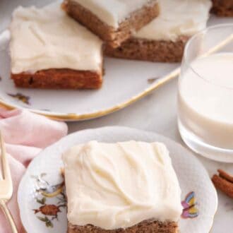 Pinterest graphic of a plate with a slice of banana bar with a glass of milk and platter of more bars in the background.