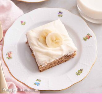 Pinterest graphic of a plate with a serving of banana bar with sliced bananas on top. Glass of milk to the side.