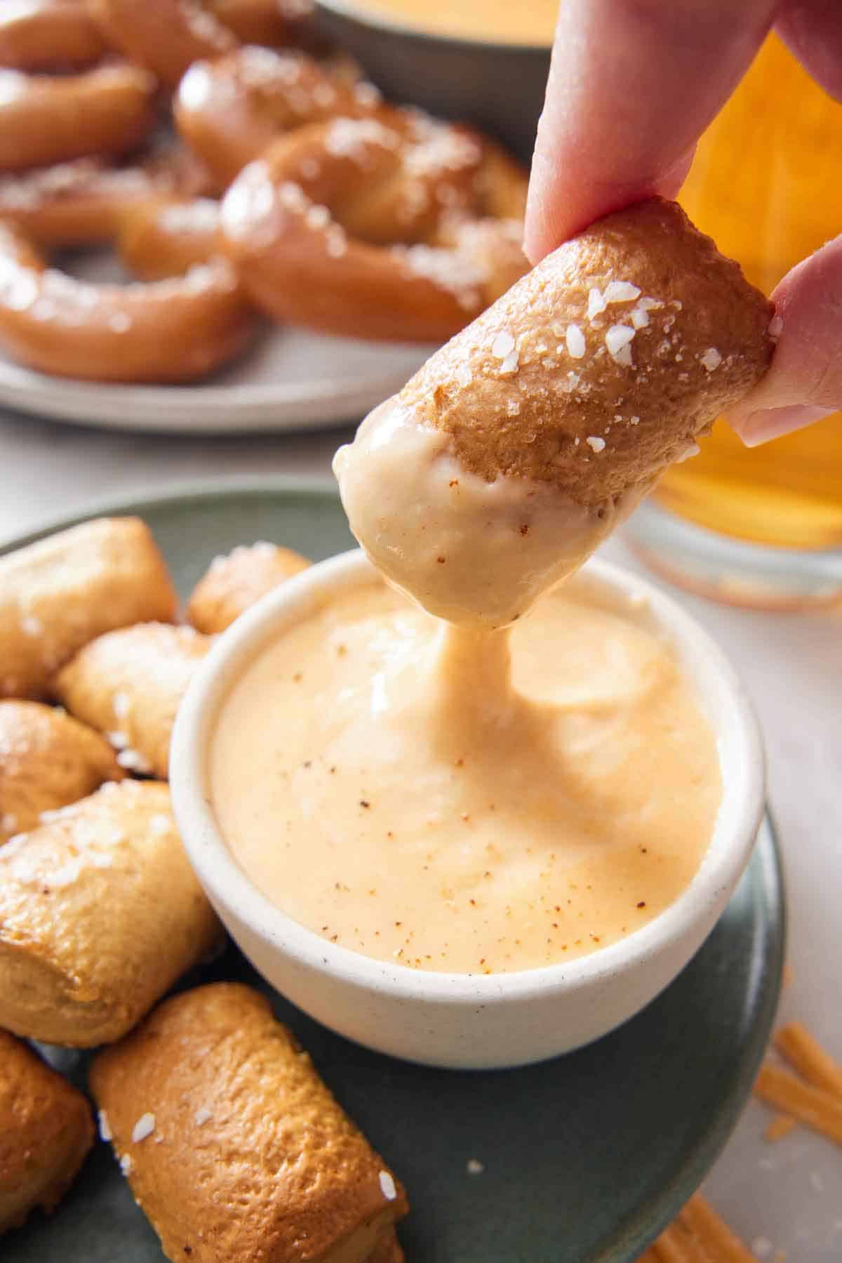 A pretzel bite dipped into a bowl of beer cheese dip.