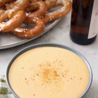 Pinterest graphic of a bowl of beer cheese dip with a platter of pretzels and a bottle of beer in the background.