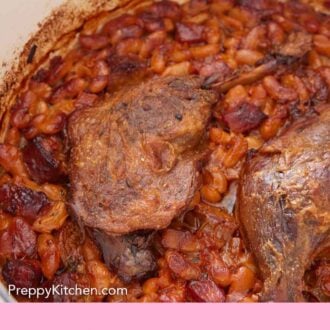 Pinterest graphic of a close view of the duck leg in a pot of cassoulet.