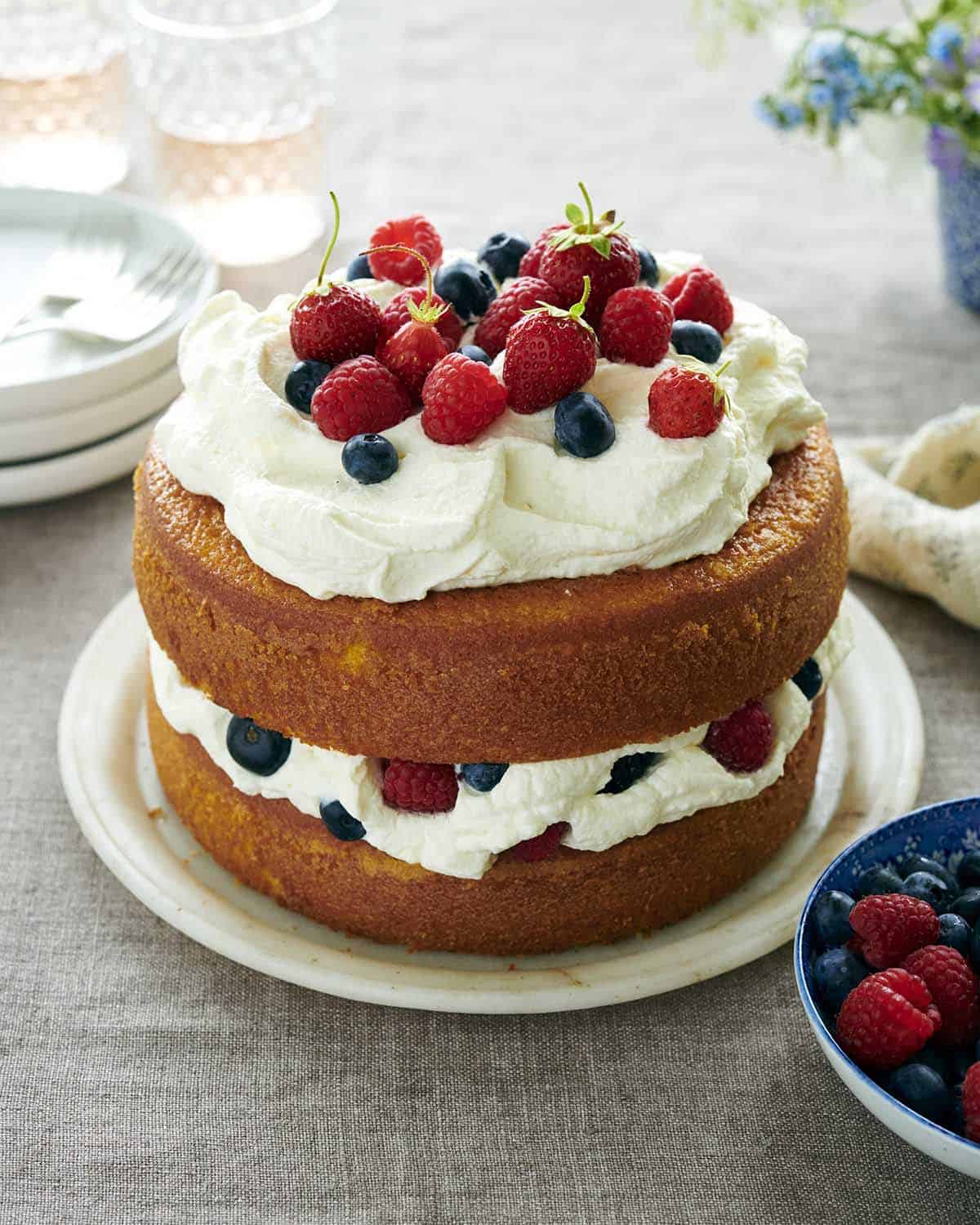 A a photo of a two layer olive oil cake with whipped cream and berries on a table.