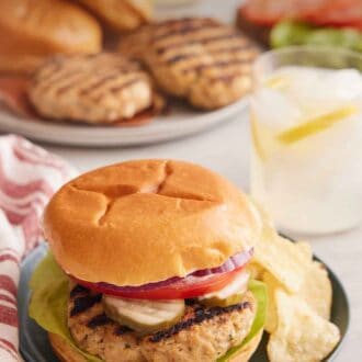 Pinterest graphic of a plate with a chicken burger with potato chips with a drink in the background and burger components on plates.
