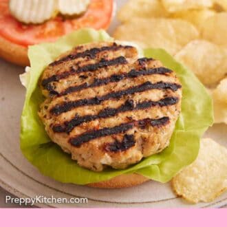 Pinterest graphic of a grilled chicken burger on top of lettuce on a bun. Chips in the background and the rest of the burger in the back.
