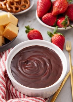 A bowl of chocolate fondue with assorted dippers in the background.