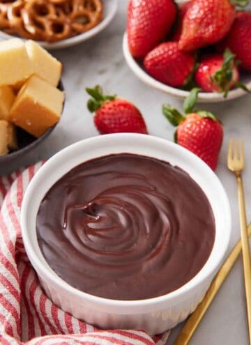A bowl of chocolate fondue with assorted dippers in the background.